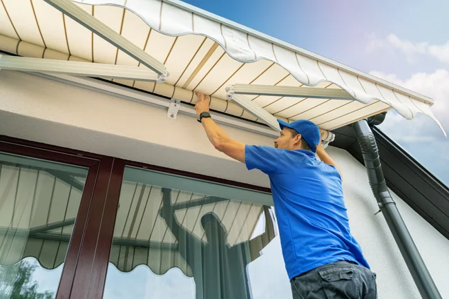 Técnico instalando toldo retrátil bege na fachada de uma casa